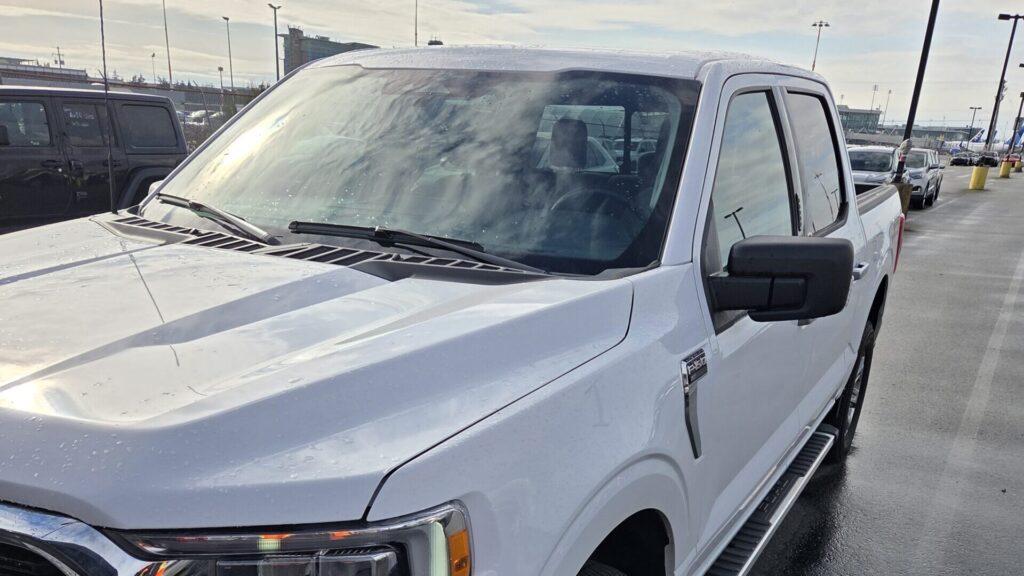 White Ford F-150 parked on a wet lot under a partly cloudy sky.