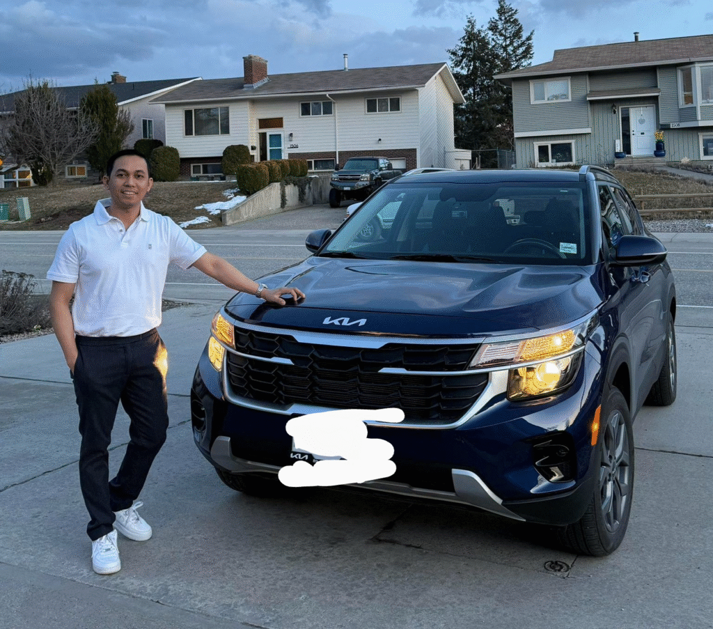Smiling man standing proudly beside a new dark blue Kia SUV in a residential Canadian neighborhood.
