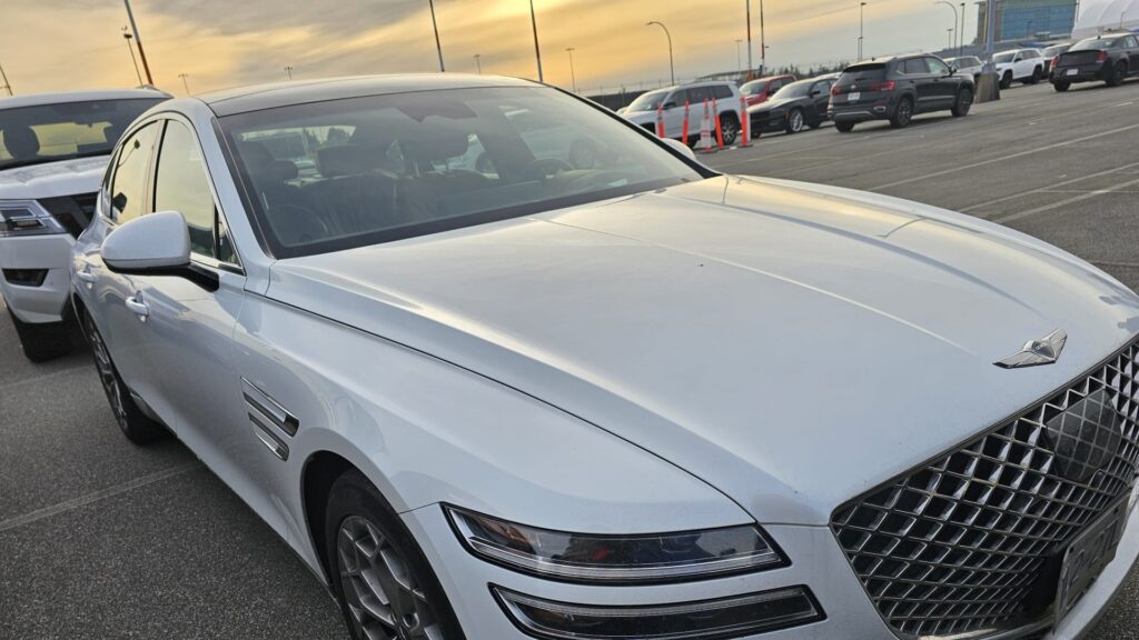 White Genesis luxury sedan parked in outdoor lot at sunset, front-side angle view