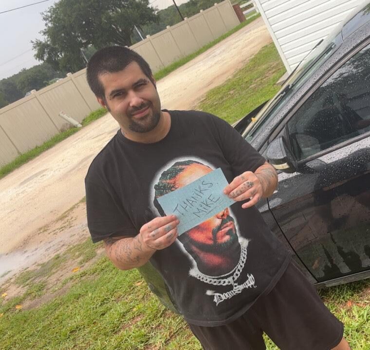 Smiling man holding a "Thanks Mike" sign in front of his newly purchased black car