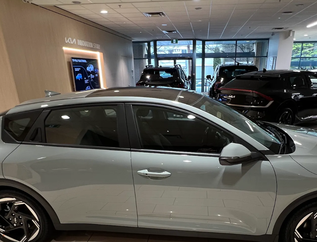 A light gray Kia EV on display in a bright dealership showroom.