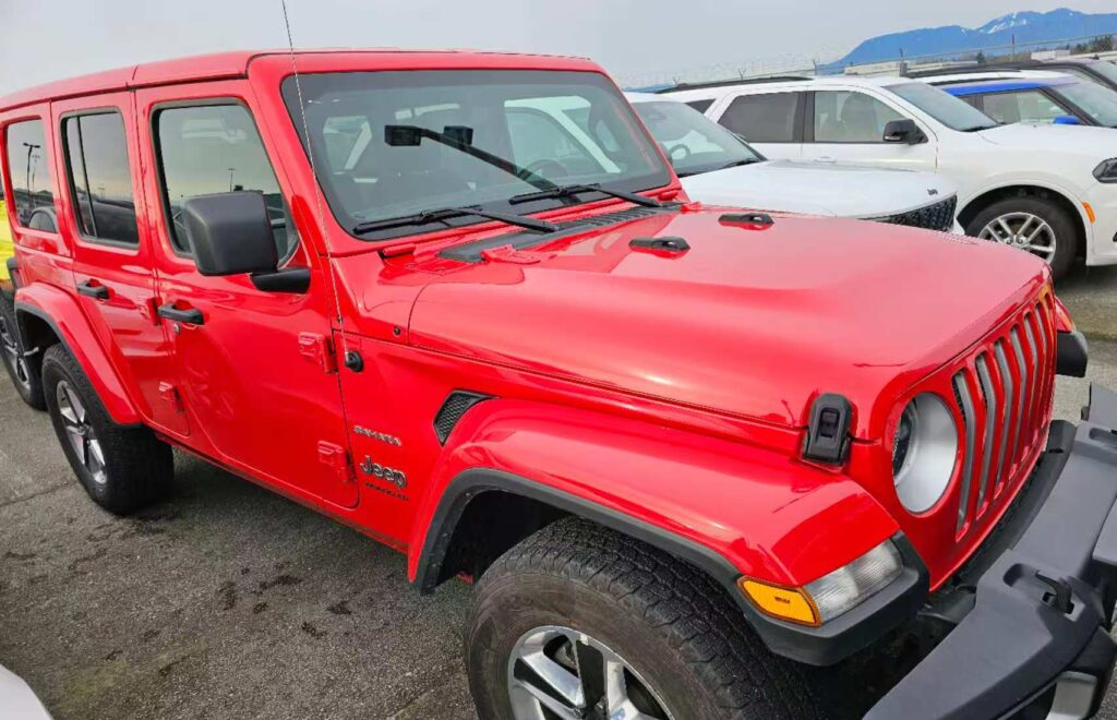 Bright red Jeep Wrangler parked in a dealership lot, ready for adventure.